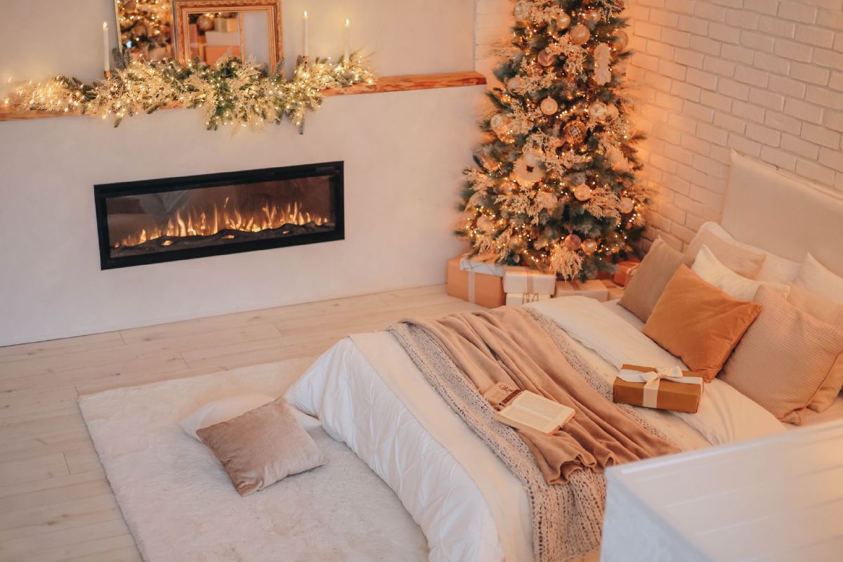 Warm and inviting Christmas-themed bedroom with a decorated tree beside a garland-draped mantel and fireplace
